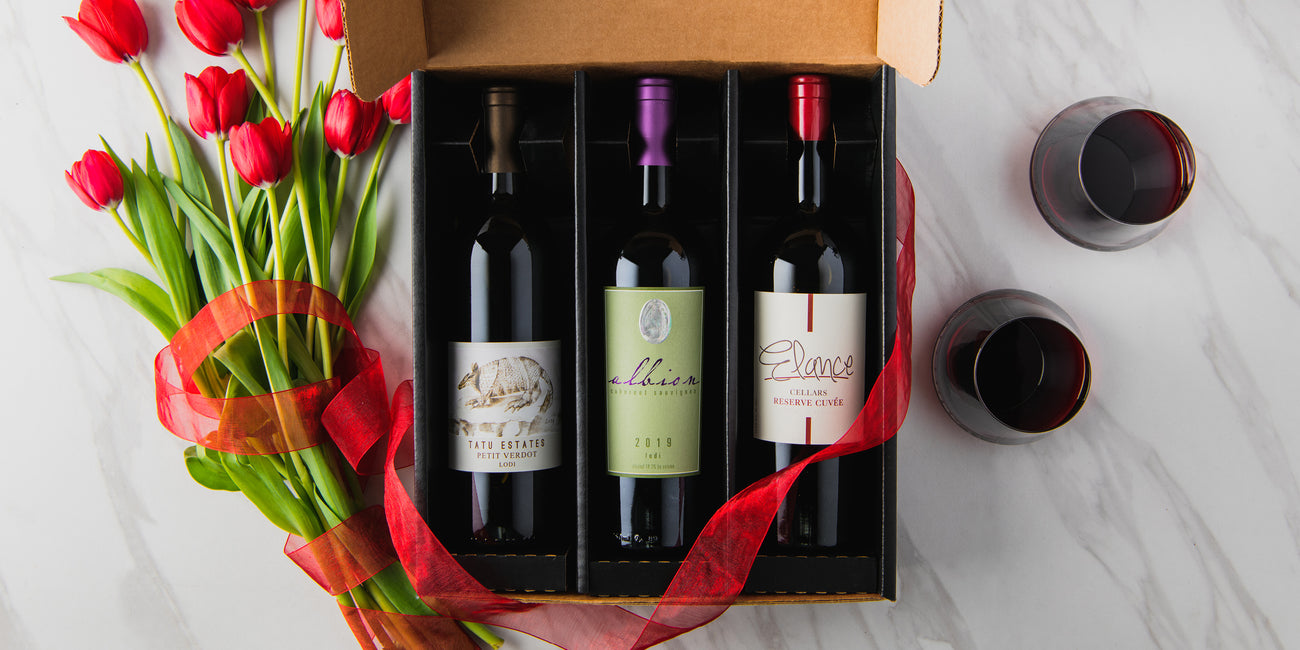 Three bottles of wine in a box with a bouquet of tulips on a marble surface.