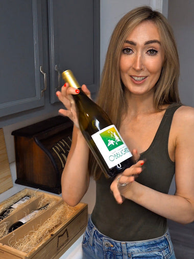 Woman holding a wine bottle with a label in a kitchen setting