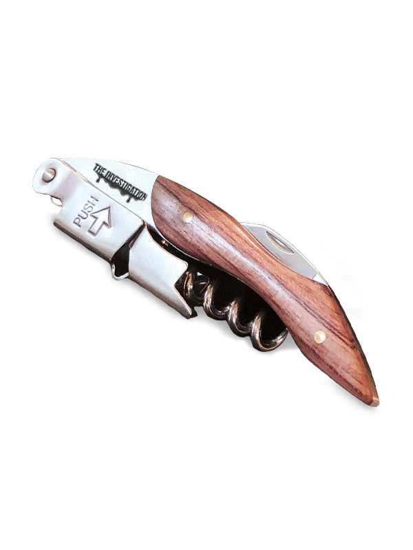 A corkscrew opener with a polished reddish-brown wooden handle and a silver metal blade, shown open on a plain white background. The blade features the engraved brand name 'THE INVESTIGATION"