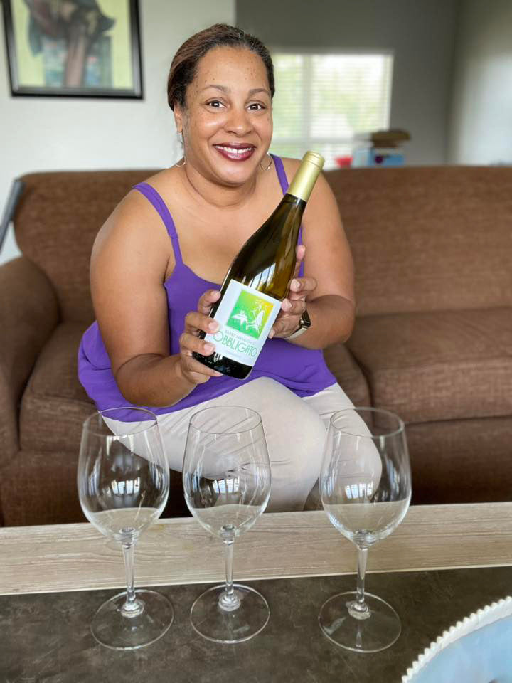 Woman holding a wine bottle with three empty glasses on a table in a living room setting.