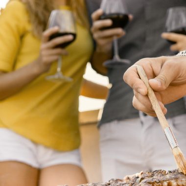 People holding wine while grilling ribs