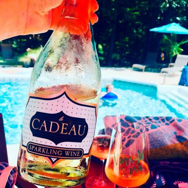 A bottle of Cadeau Semi-Seco Sparling Wine being held up during a pool party