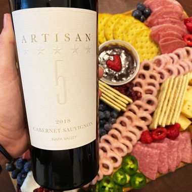 Person holding bottle of Artisan 5 with platter of snacks