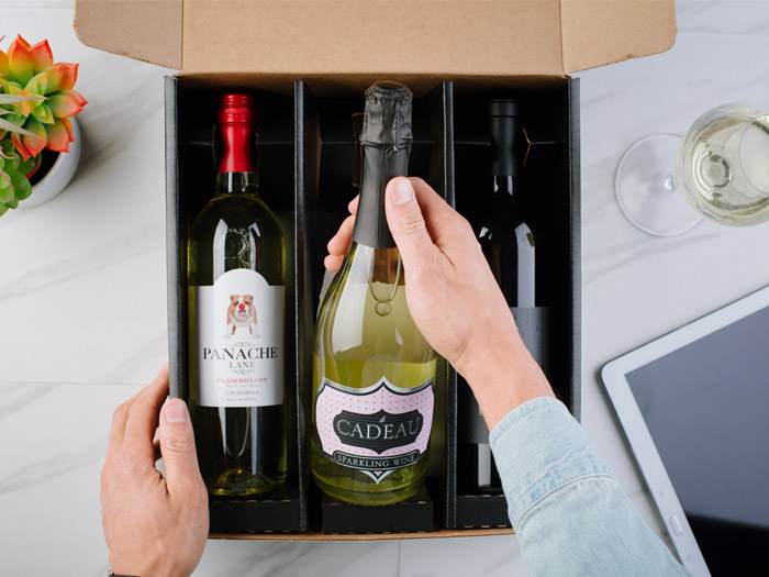 Man opening box of 3 wines with a glass of wine and a tablet beside it