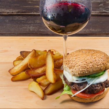 Glass of wine with burger and fries on wooden board