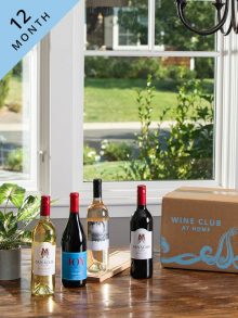 2 white and 2 red WineShop At Home wines for 12-Month Wine Club displayed on kitchen table with the Wine Club box.