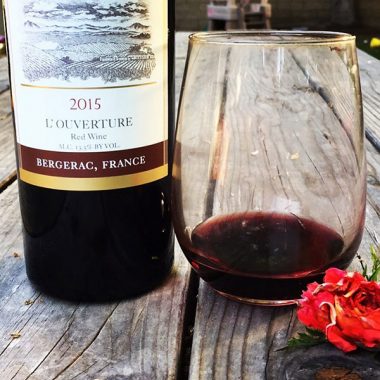 A close up of a bottle of Terroir Cellars 2015 L'Ouverture and filled glass on an outdoor picnic table