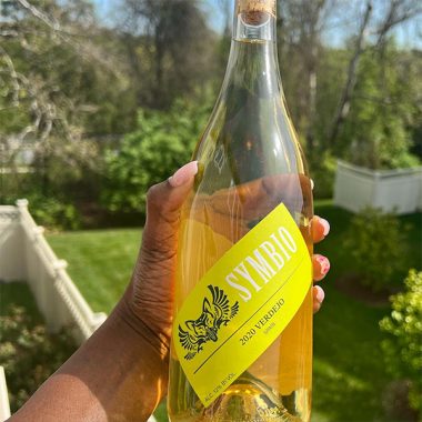 A close up of a bottle of Symbio 2020 Verdejo being held on a balcony overlooking a yard