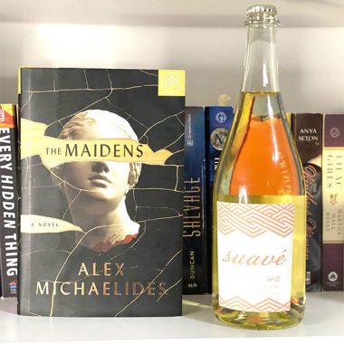 A bottle of Suavé Wiz Sparkling Wine next to a hard cover copy of "The Maidens"
