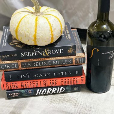 A bottle of Somersville Cellars 2020 Meritage next to a stack of books with a small yellow pumpkin on top of them
