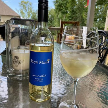 A chilled filled glass of Royal Mama Mimi's Blend next to a bottle on an outdoor patio table