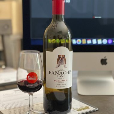 A bottle of Panache Lane Bodacious with a WineShop At Home mini wine glass placed on a Tasting Menu in front of an iMac