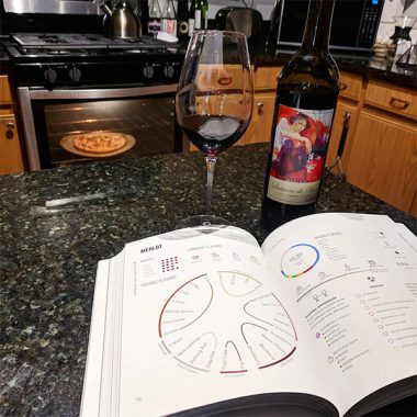 A bottle of Lumière de Vie Merlot next to a semi-filled glass and a wine book on a kitchen island