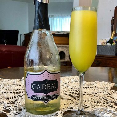 A chilled bottle of Cadeau Semi-Seco Sparkling Wine next to a mimosa on a living room table