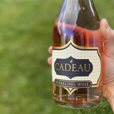 Close up of the label of a bottle of Cadeau Rosé Sparkling Wine outdoors in front of grass
