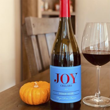 A bottle and glass of Joy Cellars 2018 Pinot Noir next to a mini pumpkin on a wooden table