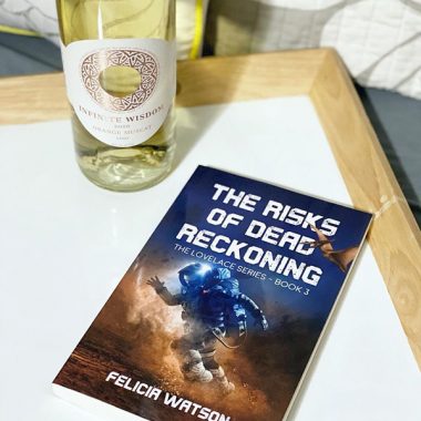 A bottle of Infinite Wisdom 2020 Orange Muscat next a paperback copy of "The Risks of Dead Reckoning" on a serving tray