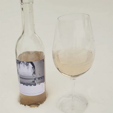 A bottle of Homage Cellars 2019 Pinot Grigio and filled glass in the snow