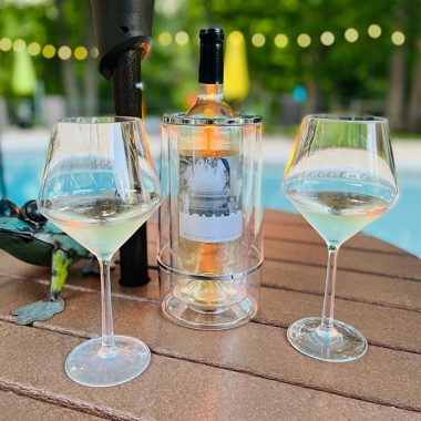 A bottle of Homage Cellars with two filled glasses on a table in front of a pool