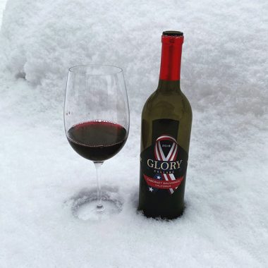 A bottle of Glory Cellars 2018 Cabernet Sauvignon and filled glass in the snow