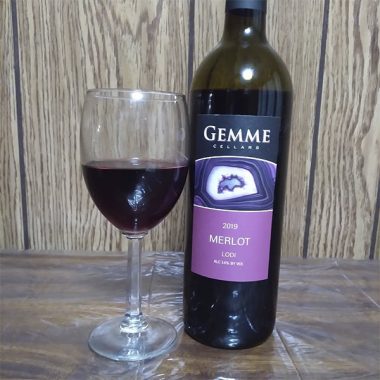 A bottle of Gemme Cellars 2019 Merlot next to a filled glass