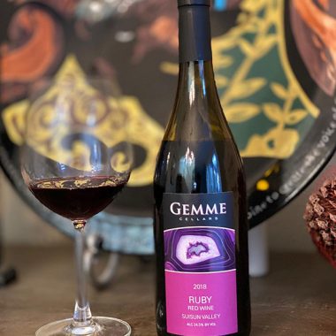 A bottle of Gemme Cellars 2018 Ruby next to a filled glass in front of some porcelain plates