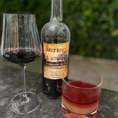 A mixed cocktail next to a filled glass and bottle of Family Ranch Aged 3 Months on Bourbon Oak Red Wine