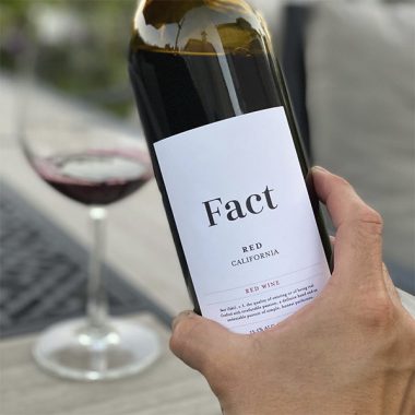 A close up of Fact Red Wine in front of a filled glass outside