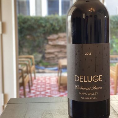 A bottle of Deluge 2012 Cabernet Franc on a kitchen table overlooking backyard