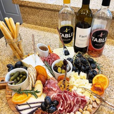 Charcuterie board with cheeses and various snacks and three bottles of wine